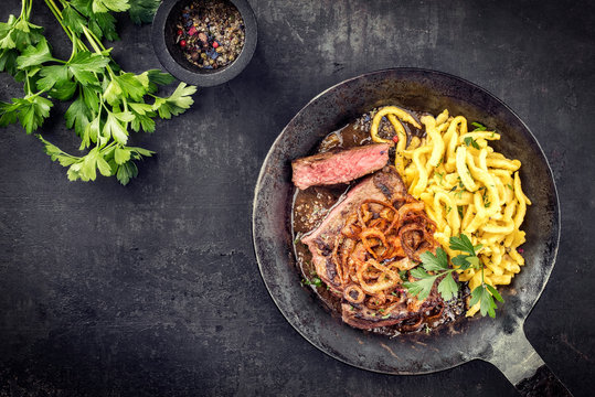 Traditional dry aged sliced roast beef with fried onion rings and Swabian spaetzle as top view in a wrough-iron pan with brown sauce
