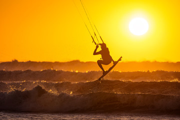 Silhoutte of kitesurfers enjoying big waves at sunset in Essaouira, Morocco. Beautiful landscape in background