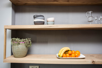 Fototapeta na wymiar Shelf with various things and fruits on the table, green plant and glasses grey wall
