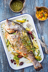 Fresh barbecue gilthead seabream with mango chutney and chimichurri as top view in a white skillet
