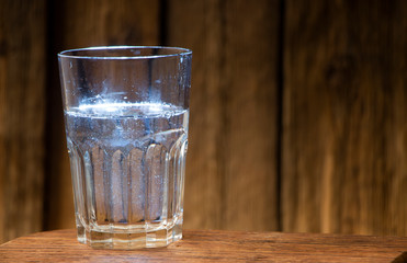 Glass of water on a wooden table against the background of a wooden wall