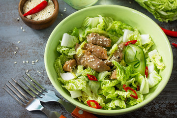 Diet menu. Healthy salad with Chinese cabbage, chicken, sesame and chili pepper on a dark stone table. Copy space.