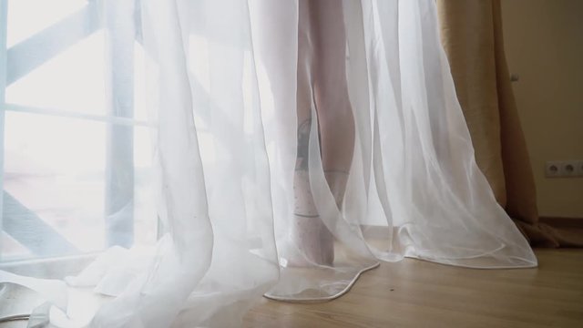 A woman throws her nightie on the floor standing near a large bright window. Naked woman in the bedroom.