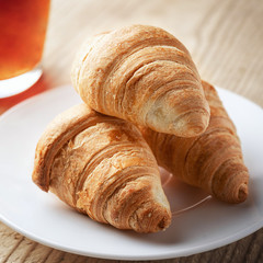 Three croissants on a white plate next to a Cup of tea