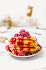 Stacked pancakes with fresh berries and icing sugar on light background