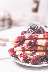 Stacked pancakes with fresh berries and icing sugar on light background