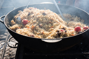 Tasty Uzbek pilaf in a cauldron on fire in the open air at street food festival