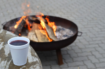 Tisch mit Becher voller Gl&uuml;hwein im Hintergrund ein Feuer