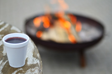 Tisch mit Becher voller Glühwein im Hintergrund ein Feuer