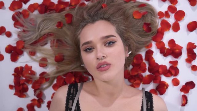 Portrait of a young girl with a piercing on which fall red rose petals close up. Slow motion.