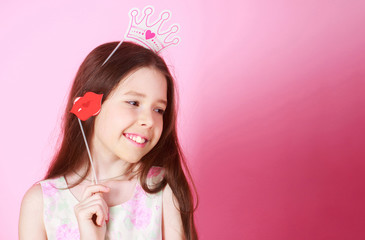 Little girl princess, lip, crown, isolated on pink background. Celebrating carnival for kids, birthday party. Cute little girl in a princess costume, lips. Child preparing for a party. Copy space.