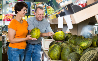 Fototapeta premium Glad man and his wife are choosing ripe melon