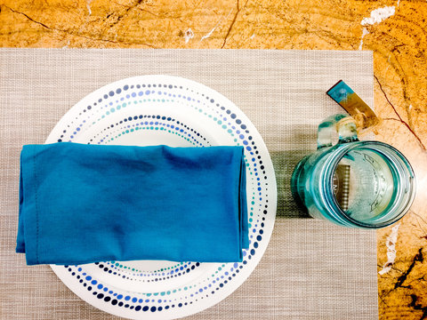 Blue napkin, plates, mason jar on a wooden table on a cloth mat. This setting  is perfect for modern homes with young residents or on the holidays