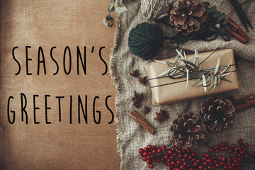 Season's greetings text sign on stylish rustic christmas gift box with fir branches, red berries, pine cones, cinnamon on rustic wood. Atmospheric image. Seasonal greeting card © sonyachny