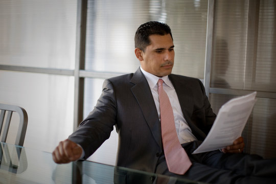 Mid-adult businessman sitting and reading documents in an office.