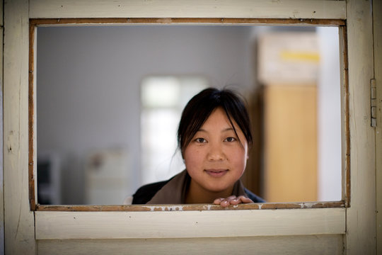 Portrait of woman peering through at gap at the top of a door.