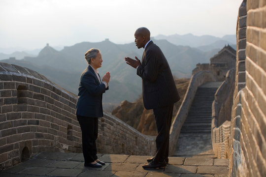Chinese businessman and woman greeting each other traditionally at the Great Wall of China.