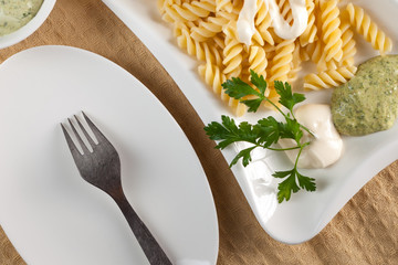 Pasta in white plate, parsley, bowl with mayonnaise sauce