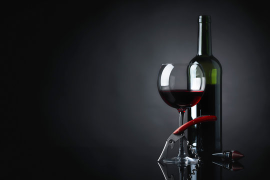 Red wine with corkscrew on a black background.