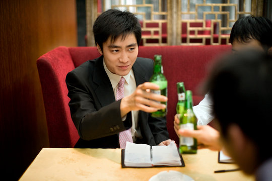 Young adult businessmen sitting at a table in a bar toasting beers.