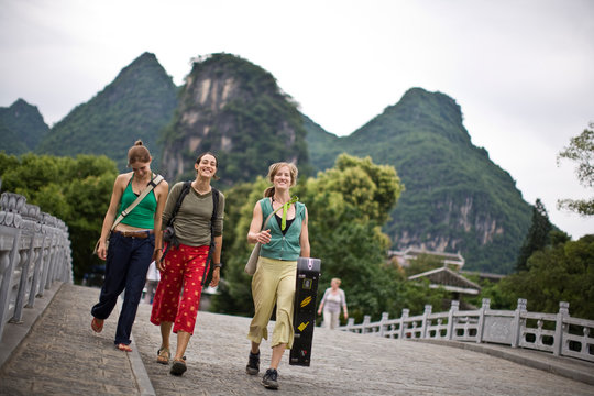 Portrait of three smiling female tourists walking along an urban street.