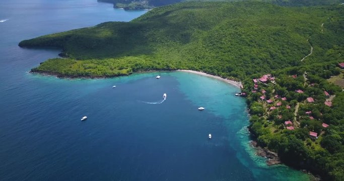 Drone flying over a Tropical paradise beach surrounded by water and rainforest in the Caribbean sea with boats