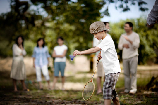 Young boy playing badminton outdoors.