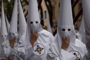 Hooded dressed in white in procession, hold the hood against the wind