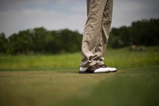 Man wearing golf shoes on a golfing green.