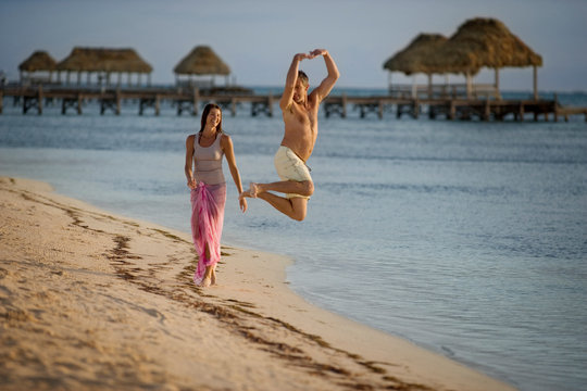 Man doing a pirouette on the beach with his partner laughing