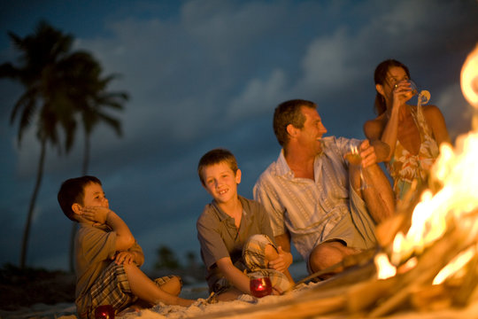 Portrait of a young boy sitting with his parents and younger brother on a beach next to a fire.