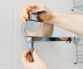 Plumber hands fixing shower mixer on modern water tap.