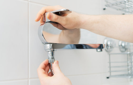 Plumber hands fixing shower mixer on modern water tap.