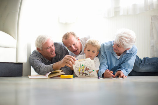 Young boy sitting on the floor with his grandparents and father while coloring in.