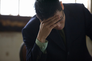 Despairing young businessman sitting with his hand on his forehead.