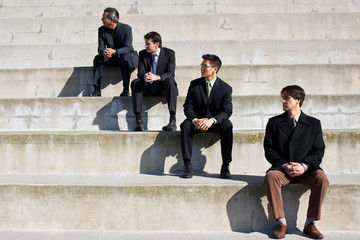 Four businessmen sitting on steps outside a building.