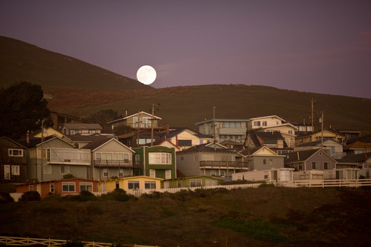 Full moon appearing above row of houses 
