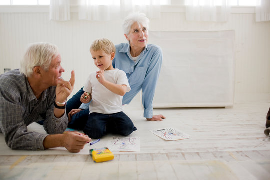 Senior couple sitting on the floor playing with their young grandson.