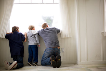 Father and his two sons looking outside a window.