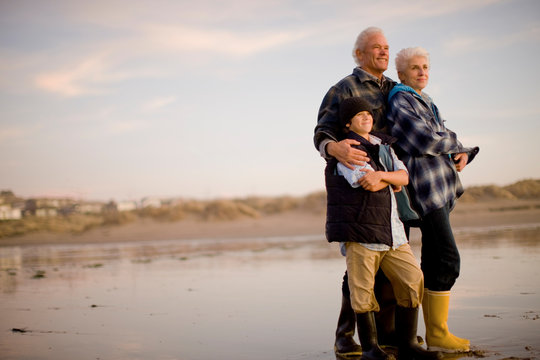 Mature adult couple standing with their teenage grandson on a beach at sunset.