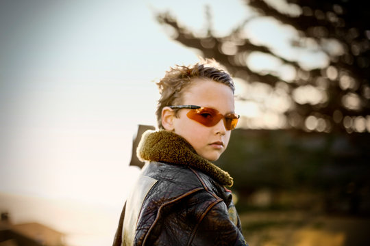 Portrait of a young boy looking over his shoulder while wearing tinted sunglasses.