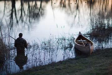 Man holding a shotgun in the water next to a canoe.