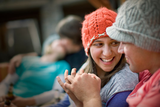 Happy young couple smiling at each other with their hands intertwined while a couple kiss behind them.