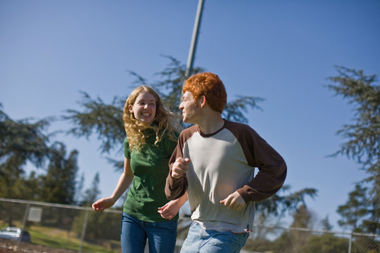 Laughing teenage couple looking at each other while running side by side in the sun.