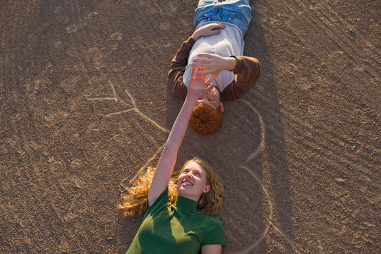 Smiling teenage couple holding hands lying on their backs on a heart shape drawn in the dirt.