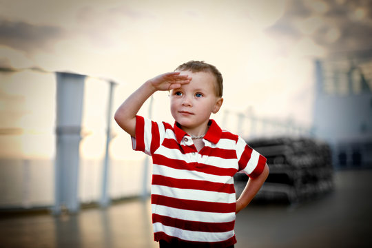 Young boy saluting while standing on the deck of a boat.