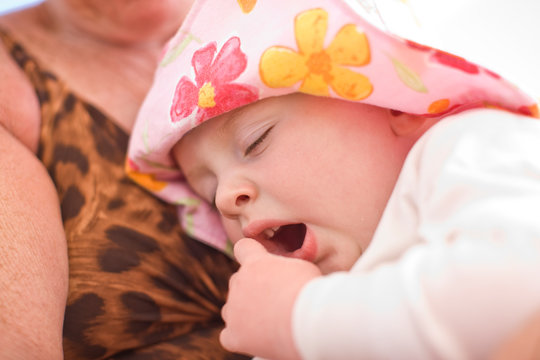 Young toddler yawning while wearing a floral sunhat.