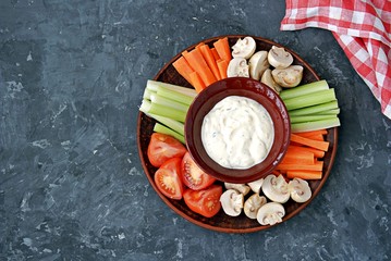 Vegetable tray with a ranch dip on a dark background. Raw vegetable mix includes sliced mushrooms, carrots, celery, tomatoes.