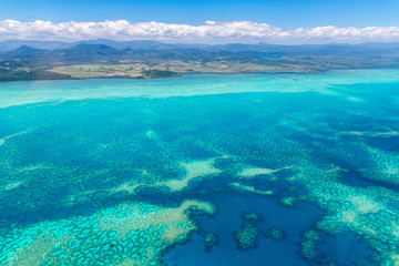 Aerial view of idyllic azure turquoise blue lagoon of West Coast barrier reef, with mountains far in the background, Coral sea, New Caledonia island, Melanesia, South Pacific Ocean. - obrazy, fototapety, plakaty