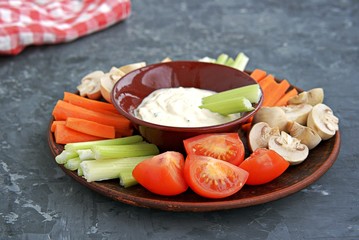 Vegetable tray with a ranch dip on a dark background. Raw vegetable mix includes sliced mushrooms,...